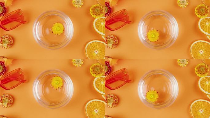 在橙色背景的一罐水里的干花。组成柑橘片、鲜花、太阳镜、香薰蜡烛、蜡菊特写、俯视图。夏天明亮的纹理工作