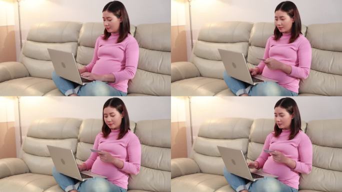 亚洲孕妇坐在沙发上，用家里的笔记本电脑享受网上购物