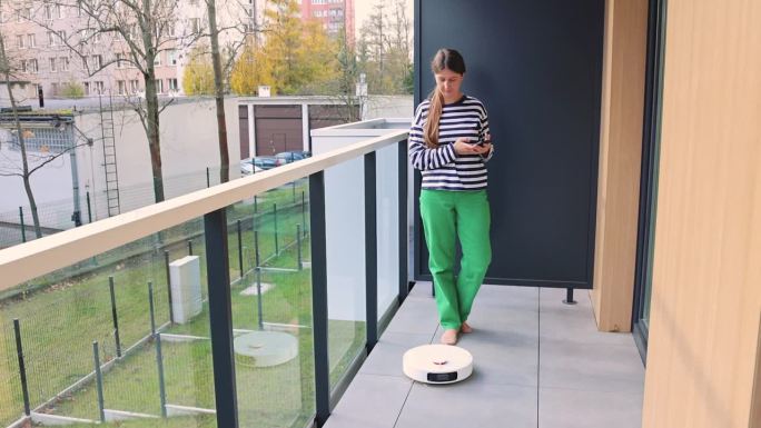 一位女士在她的现代公寓露台上使用机器人吸尘器