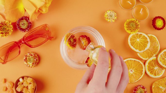 干花在一个罐子里的水和化妆品油在橙色的背景。组成柑橘片、鲜花、太阳镜、香薰蜡烛、蜡菊特写、俯视图。夏