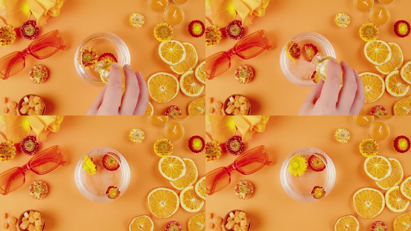 干花在一个罐子里的水和化妆品油在橙色的背景。组成柑橘片、鲜花、太阳镜、香薰蜡烛、蜡菊特写、俯视图。夏