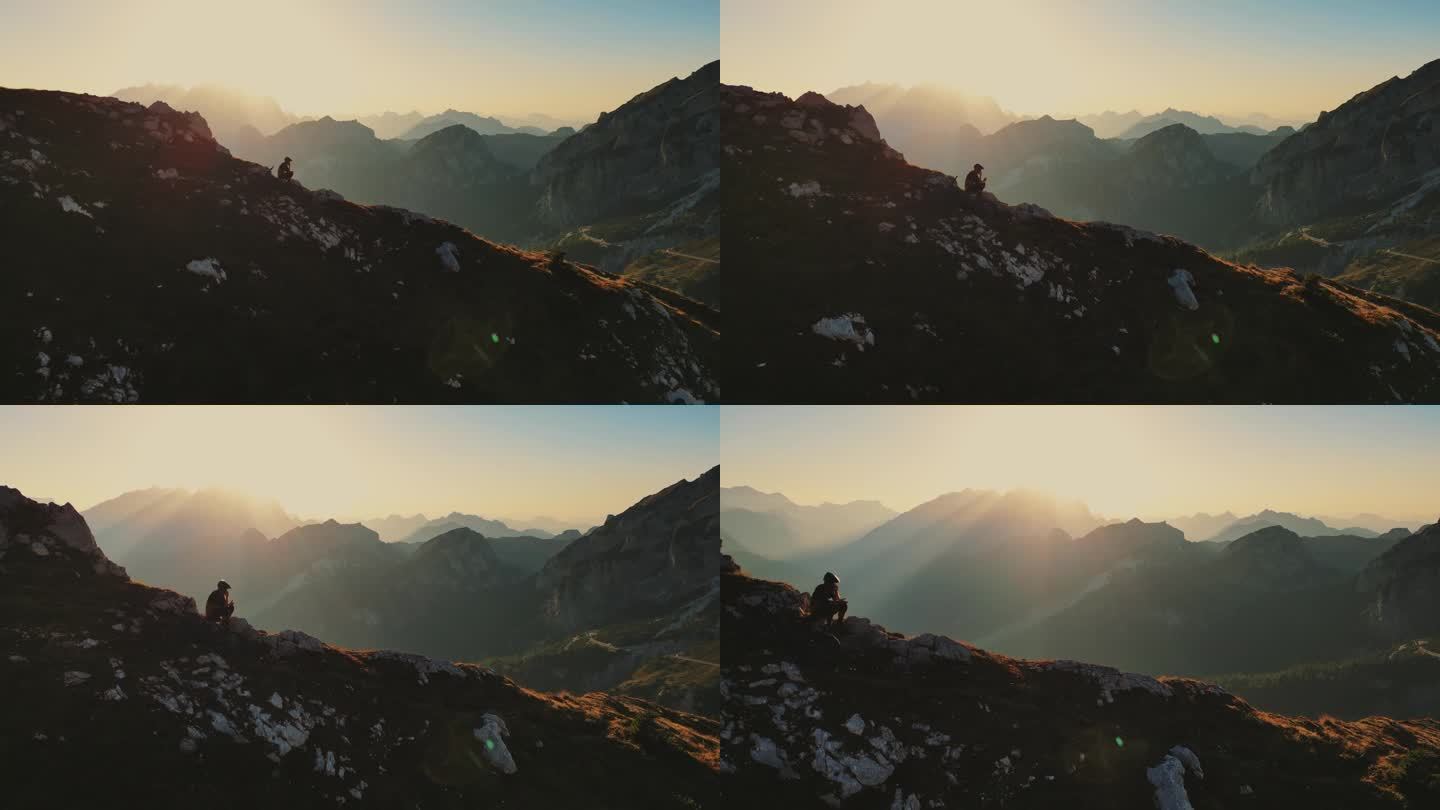 无人机拍摄的山地自行车手在阳光明媚的日子里坐在巨大的悬崖边使用智能手机的画面