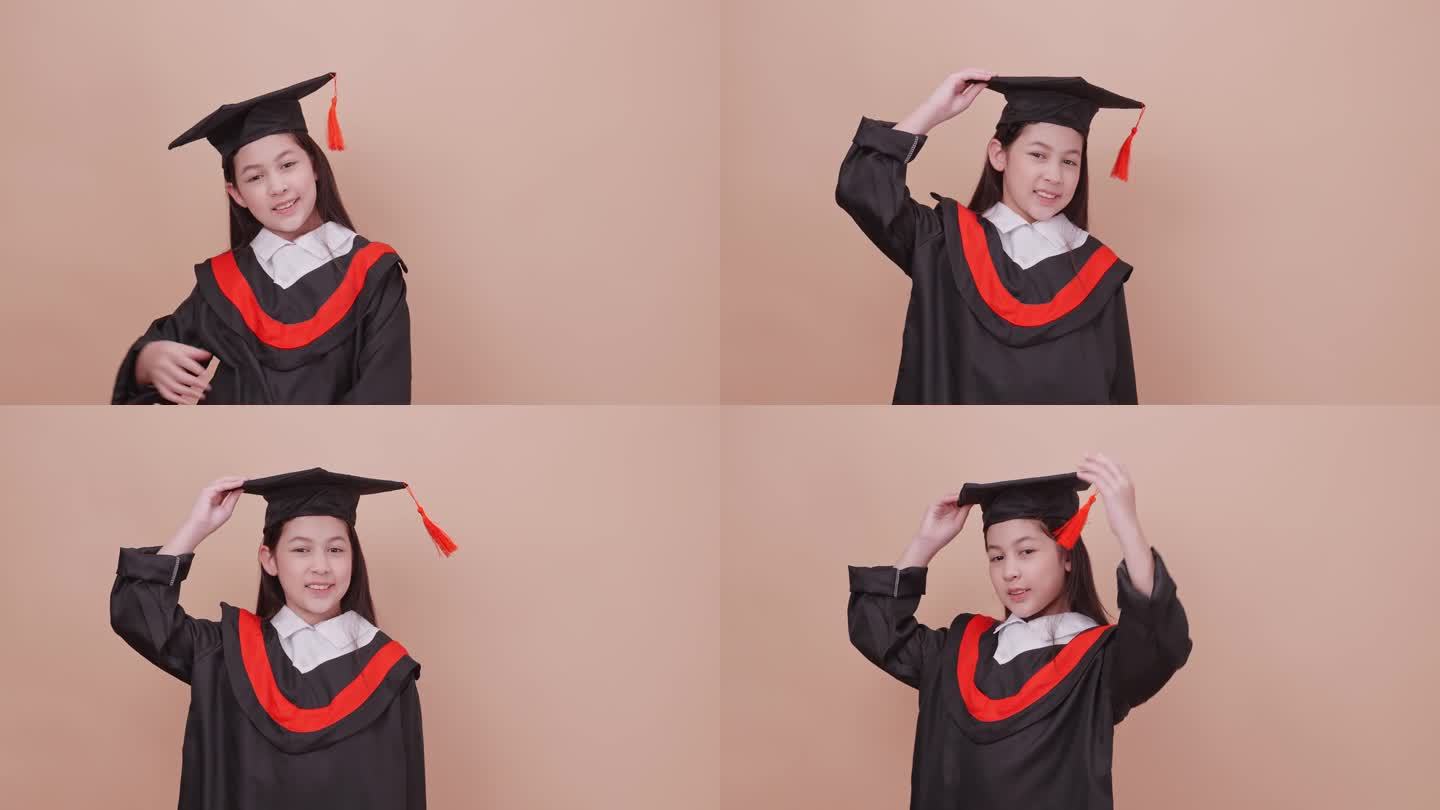 一个穿着毕业礼服的女学生做着快乐的手势和表情。孤立在褐色背景的工作室。