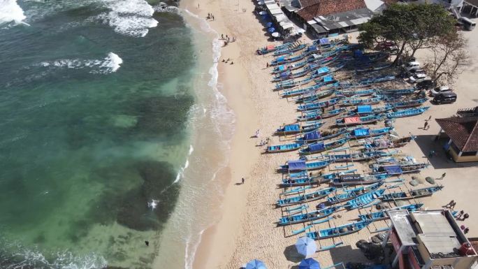 无人机拍摄的印尼日惹海滩上的雨伞、船只和度假的人们