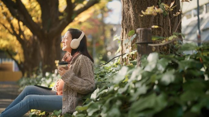 孕妇坐在公园里听音乐，喝热饮