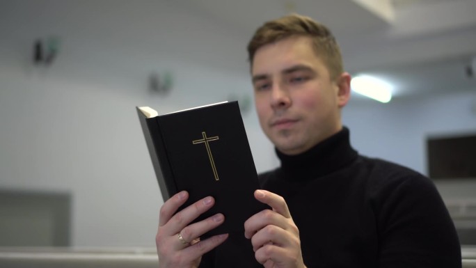 一个年轻人坐在教堂的长凳上读圣经。一个新教徒在教堂读《圣经》。4 k