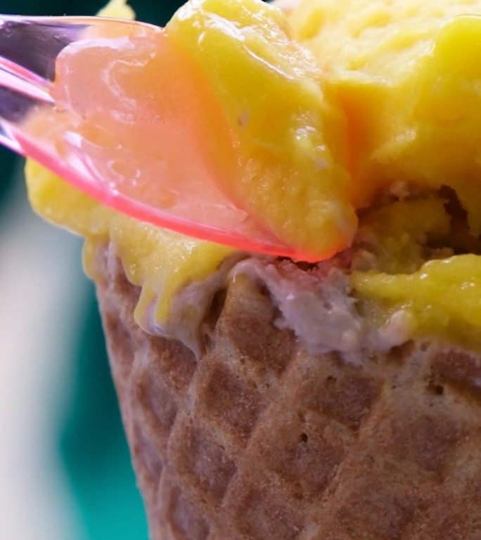 一个女人手里拿着一个白色的勺子，端起黄色的芒果冰淇淋，有人把水果冰淇淋放在威化蛋筒里，特写。在春天或