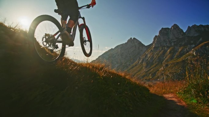 慢动作男子骑自行车越过草山对落基山脉和蓝天在阳光明媚的一天