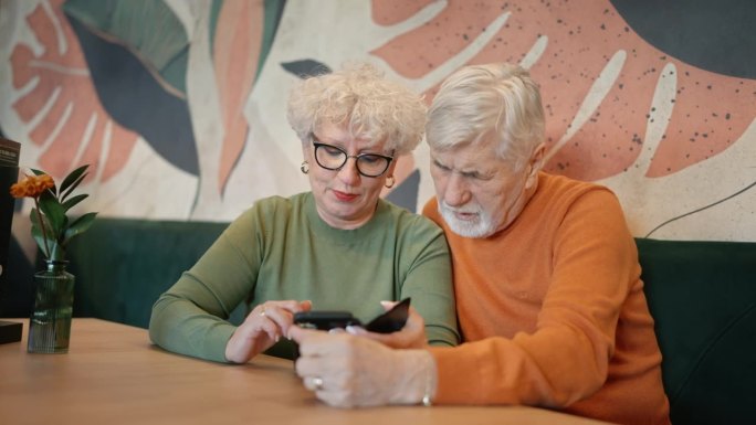 穿着便服的老夫妇在餐厅的餐桌上边玩手机边聊天