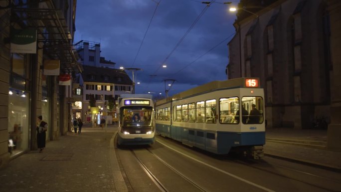 09/11/2023瑞士苏黎世。有轨电车抵达利马特奎老城区中心的车站。深夜的灯光，实时，行人游客的背