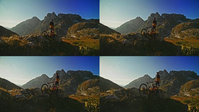 在阳光明媚的日子里，男性骑自行车的人站在落基山上，对着山脉