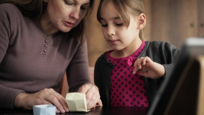 儿童女孩和母亲做折纸玩具使用彩色纸的步骤，按照指示的视频教程在数字平板电脑上