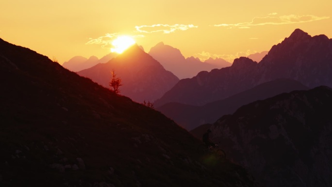 SLO MO高角度远拍的剪影摩托车站在山谷对雄伟的山脉和橙色的天空在日落
