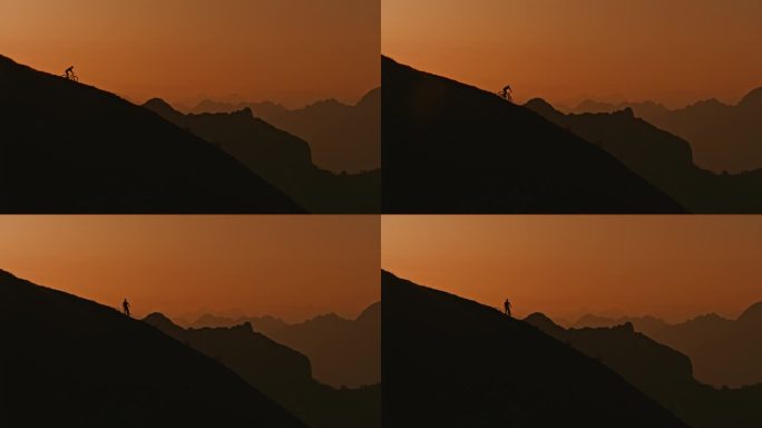 慢动作低角度远镜头的轮廓运动员骑山地车下坡对清澈的橙色天空在日落