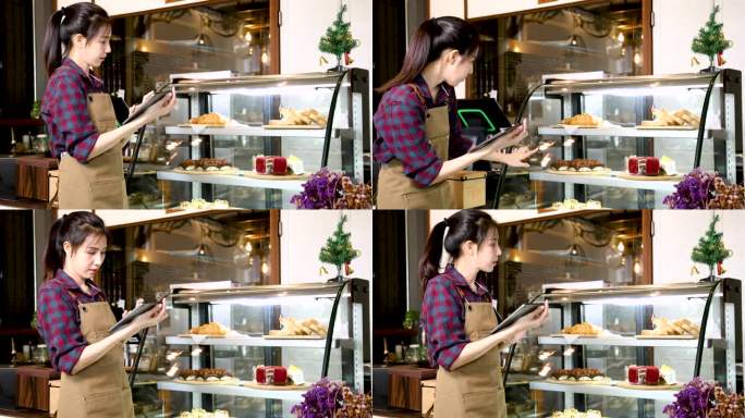亚洲创业公司女老板使用科技平板电脑面包店库存检查或点单，而站在咖啡店柜台前工作，女员工接受在线外卖