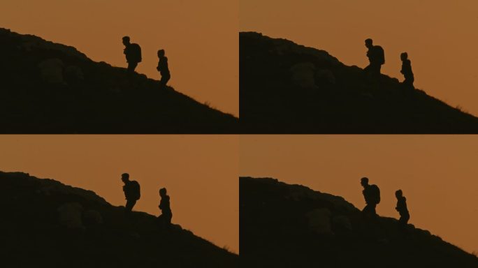 慢动作低角度手持拍摄的剪影夫妇移动上山对清澈的橙色天空在日落