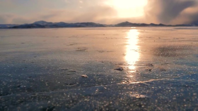 日落时分，强风吹着贝加尔湖结冰的表面上的雪晶，太阳反射在冰面上。美丽的冬季景观。