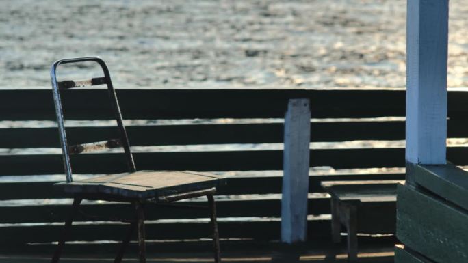 下午，在平静的大海的背景下，漂浮在房子边上的一把生锈的旧铁木椅子