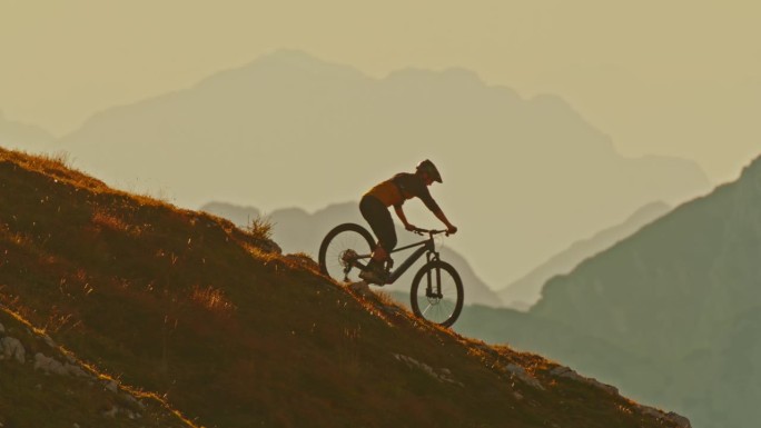 男子运动员在日落时骑山地车下坡时对雾山的侧视图