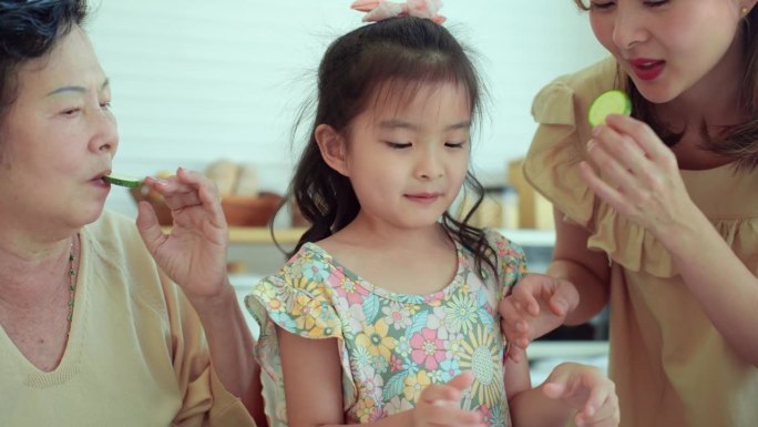 多代亚洲家庭，美丽的其他，老祖母教导和激励年轻的小女孩吃新鲜的黄瓜，这是一种营养丰富的水果，有益健康