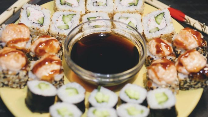 盘子里放着各式各样的寿司卷，中间放着一杯酱油。