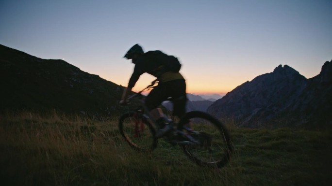 SLO MO坚定的男性自行车手在黄昏时分骑自行车对抗山脉和清澈的蓝天