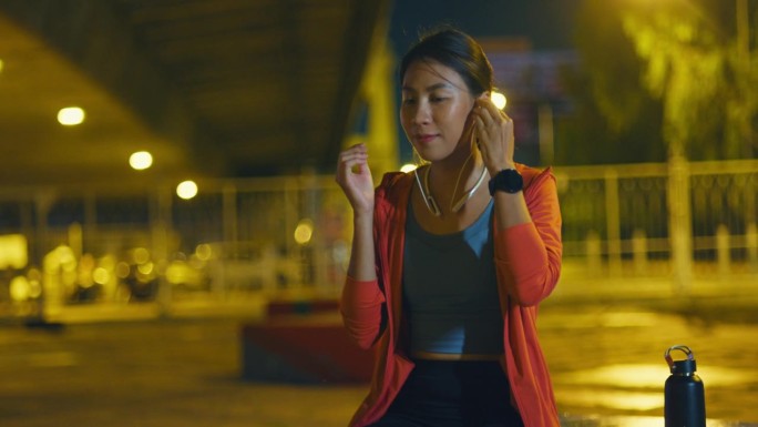 年轻的亚洲女运动员跑步者在城市夜间户外运动前，在智能手表上检查进度并查看智能手表心率监测器。健康的锻