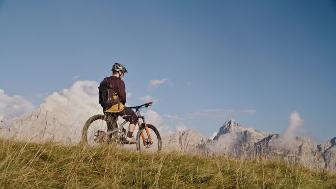 SLO - MO无人机拍摄的男性骑自行车的人在阳光明媚的日子里坐在自行车上看着落基山脉