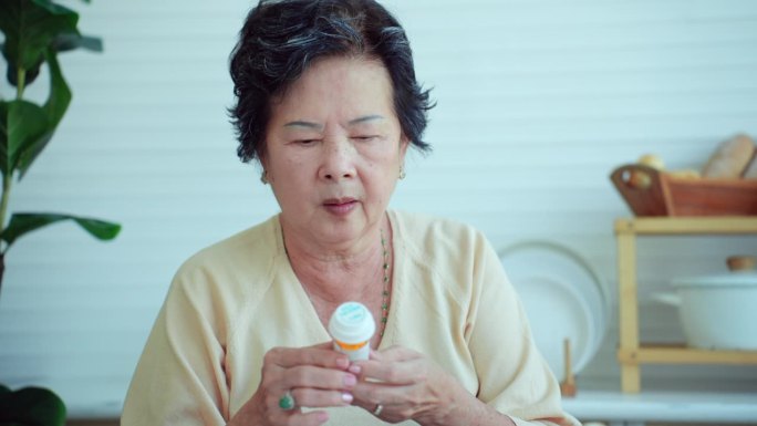 生活在温暖的家庭里，年老的亚洲祖母拿着小药瓶，里面装着治疗或预防阿尔茨海默病的日常药物胶囊。个人观点
