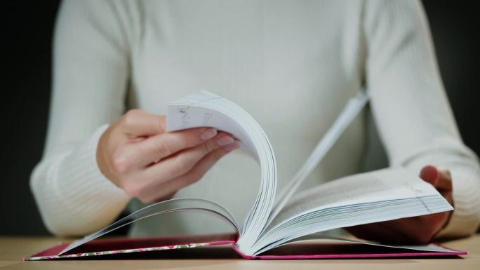 女人的手翻着西班牙语的书页，阅读和教育，翻看旧教科书。大学图书馆里的特写，微距镜头。