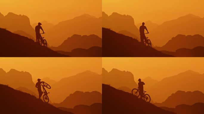 兴奋的山地车手扛着自行车站在小山上，面对雾蒙蒙的山脉和橙色的天空的剪影