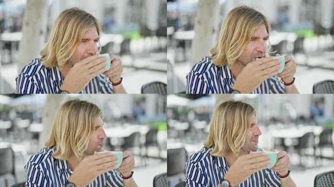 一个英俊的金发男人穿着条纹衬衫，戴着手表，在城市露台上喝着咖啡。