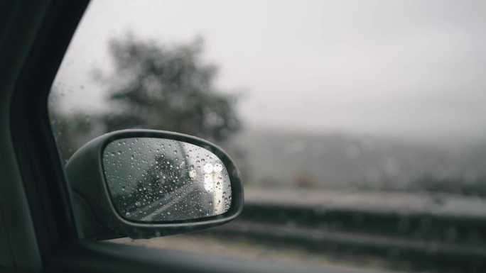 汽车在雨中行驶，镜中有雨滴和模糊的山林背景，慢动作