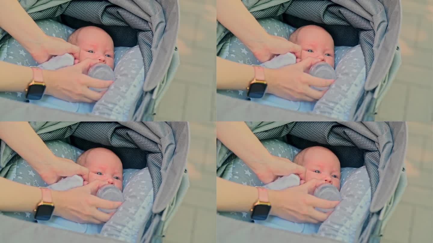 一名新生婴儿躺在婴儿车里，母亲用奶瓶喂初学走路的女婴
