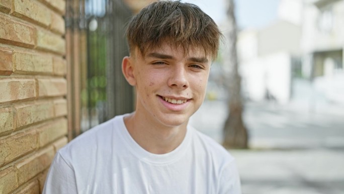一个穿着白衬衫微笑的年轻白人男性少年站在阳光明媚的城市街道上。
