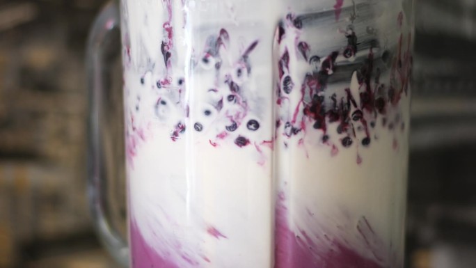 特写浆果水果掉落紫色冰沙混合在电动搅拌机。俯视图草莓蓝莓香蕉石榴落入多汁饮料超级慢动作。酸奶中的维生