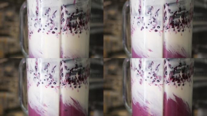 特写浆果水果掉落紫色冰沙混合在电动搅拌机。俯视图草莓蓝莓香蕉石榴落入多汁饮料超级慢动作。酸奶中的维生