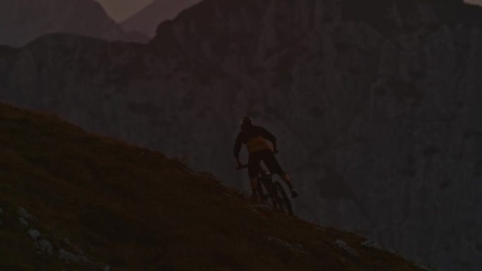 日落时分，男子山地自行车手扛着自行车在山上的SLO手持镜头