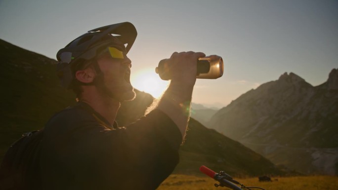 在阳光明媚的日子里，背着护具的男性骑自行车的人从瓶子里喝水
