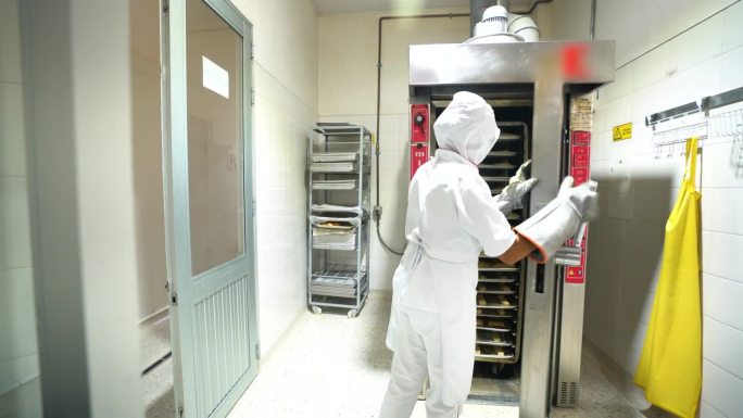 不知名的女面包师把一架子生肉馅卷饼放进工业烤箱
