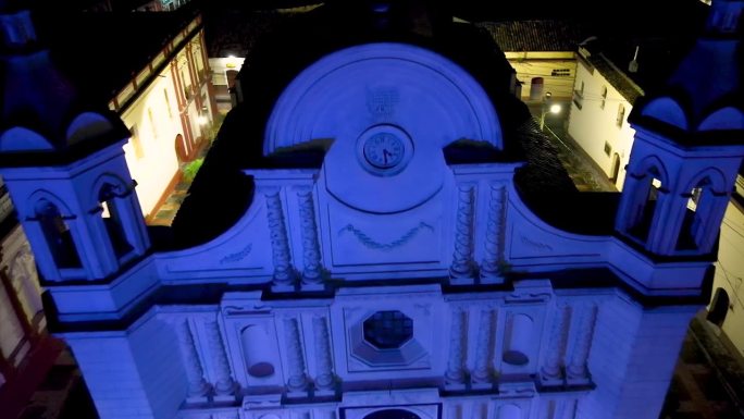在洪都拉斯圣罗莎德科潘的一座古色古香的大教堂上空拍摄的电影航拍摄影车，它被蓝色的灯光照亮