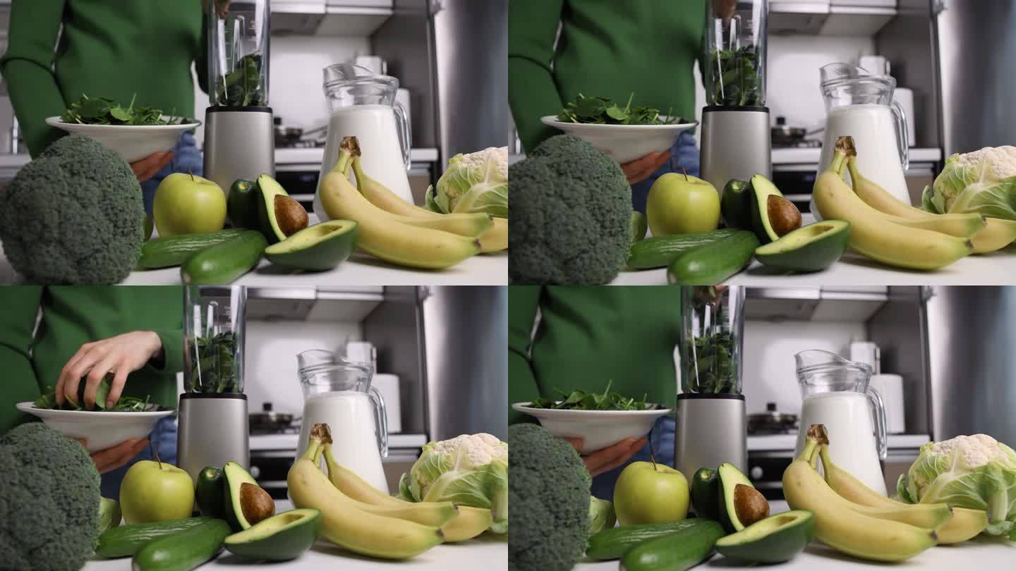 一名妇女把新鲜的绿色菠菜放在搅拌机里，在家里的厨房里用蔬菜和水果制作健康的排毒奶昔