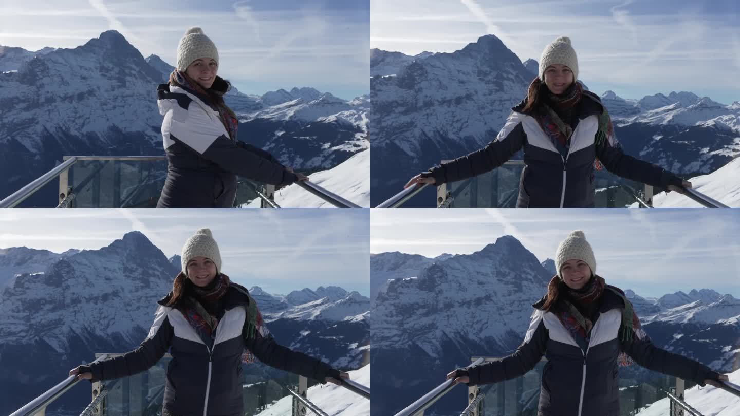 一名女子站在格林德沃第一峰的标志性平台上，俯瞰着令人惊叹的阿尔卑斯山全景，她穿着冬装，对着镜头微笑