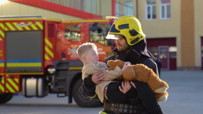 勇敢的消防员站在消防车旁，把获救的男孩抱在怀里
