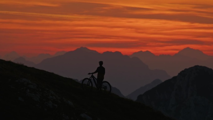 SLO MO剪影男运动员站在山上对戏剧性的橙色天空日落