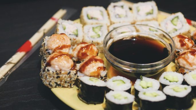 盘子里放着各式各样的寿司卷，中间放着一杯酱油。
