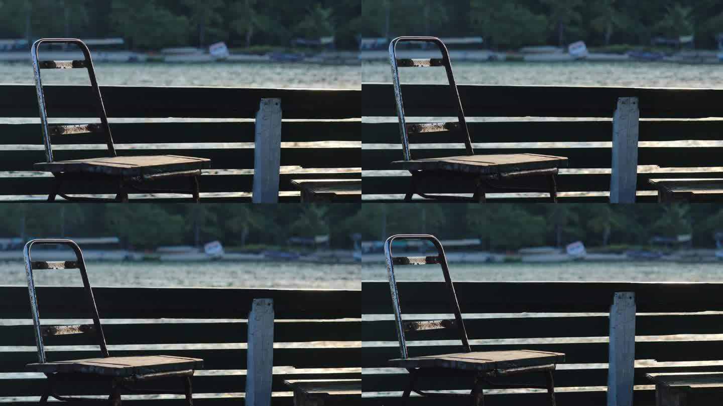 下午晚些时候，漂浮的房子边上放着一把生锈的旧铁木椅子，背景是平静的海洋和热带岛屿海滩，旁边停着一艘船