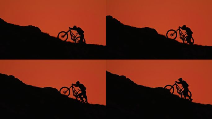 SLO MO手持拍摄的剪影山地自行车手推自行车，而移动上山对清澈的橙色天空