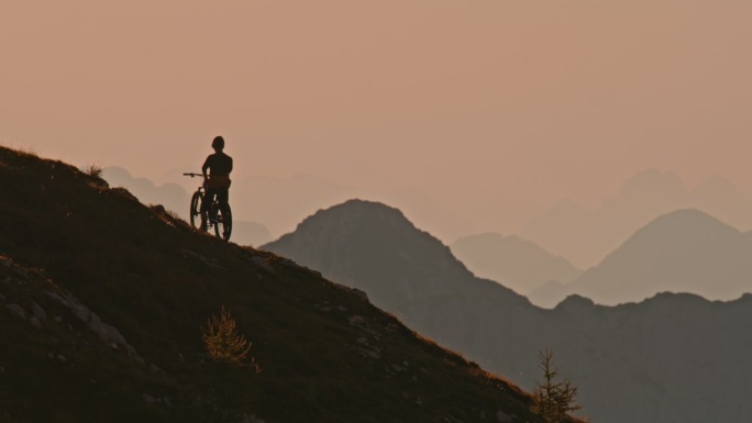 SLO MO锁定的剪影山地自行车站在山上对着晴朗的天空日落