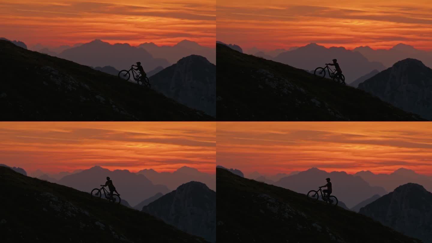 SLO MO手持镜头的轮廓男性运动员推动山地自行车上坡对戏剧性的橙色天空